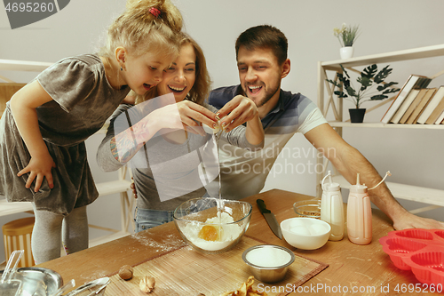 Image of Cute little girl and her beautiful parents preparing the dough for the cake in kitchen at home