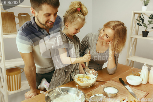 Image of Cute little girl and her beautiful parents preparing the dough for the cake in kitchen at home