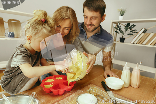 Image of Cute little girl and her beautiful parents preparing the dough for the cake in kitchen at home