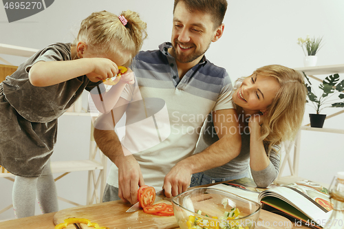 Image of Cute little girl and her beautiful parents are cutting vegetables in kitchen at home