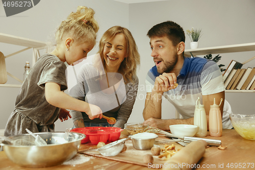 Image of Cute little girl and her beautiful parents preparing the dough for the cake in kitchen at home