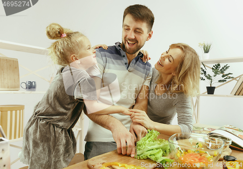 Image of Cute little girl and her beautiful parents are cutting vegetables in kitchen at home