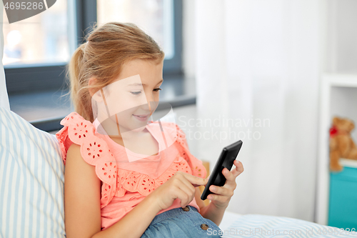 Image of girl using smartphone sitting on bed at home