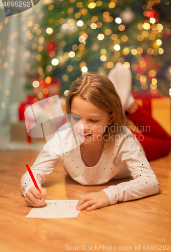 Image of smiling girl writing christmas wish list at home