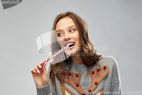 Image of woman in christmas sweater eating candy cane