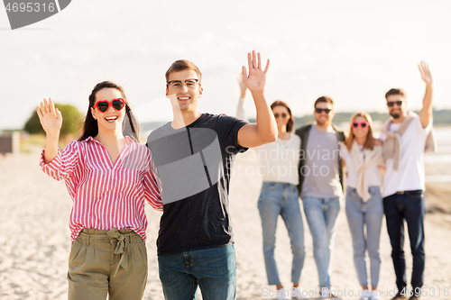 Image of happy couple with friends waving hands on beach
