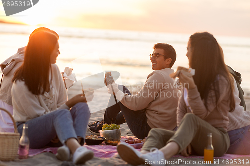 Image of happy friends eating sandwiches at picnic on beach