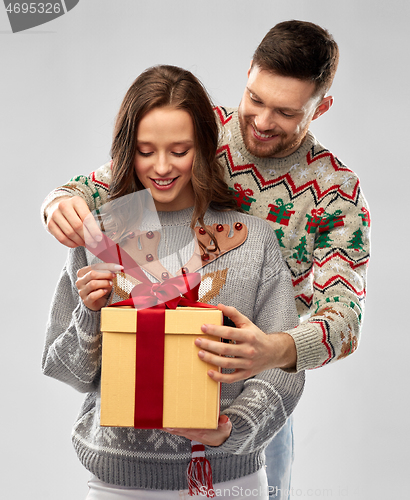 Image of happy couple in christmas sweaters with gift box