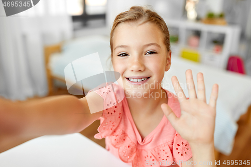 Image of happy girl taking selfie and waving hand at home