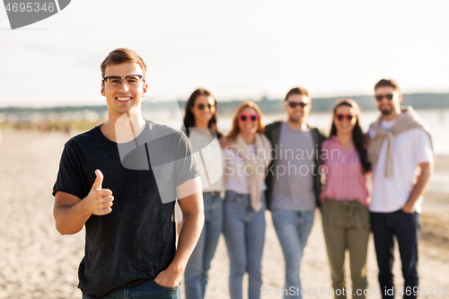 Image of happy man with friends on beach showing thumbs up