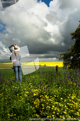 Image of Country womanat farm gate watches the clouds over golden crops a