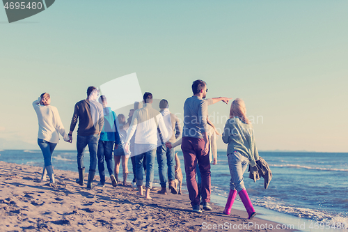 Image of Group of friends running on beach during autumn day