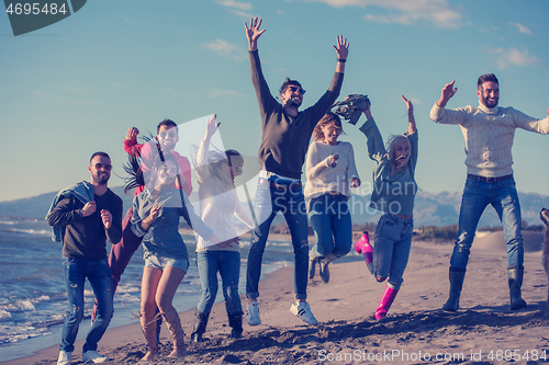Image of young friends jumping together at autumn beach