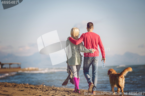 Image of couple with dog having fun on beach on autmun day