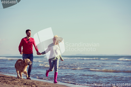 Image of couple with dog having fun on beach on autmun day