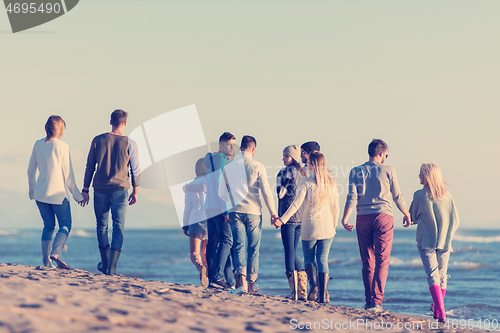 Image of Group of friends running on beach during autumn day