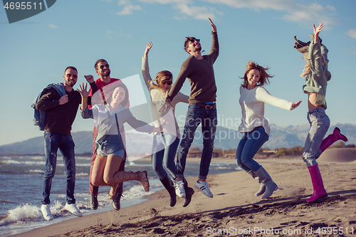 Image of young friends jumping together at autumn beach