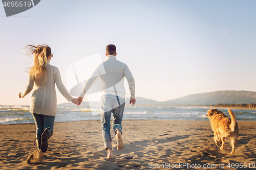 Image of couple with dog having fun on beach on autmun day