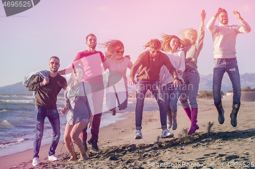 Image of young friends jumping together at autumn beach