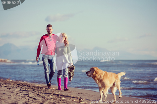 Image of couple with dog having fun on beach on autmun day