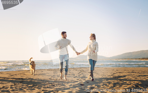 Image of couple with dog having fun on beach on autmun day