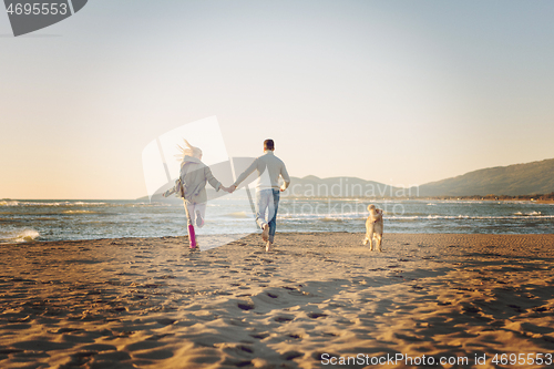 Image of couple with dog having fun on beach on autmun day