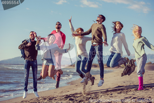 Image of young friends jumping together at autumn beach