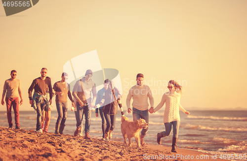 Image of Group of friends running on beach during autumn day