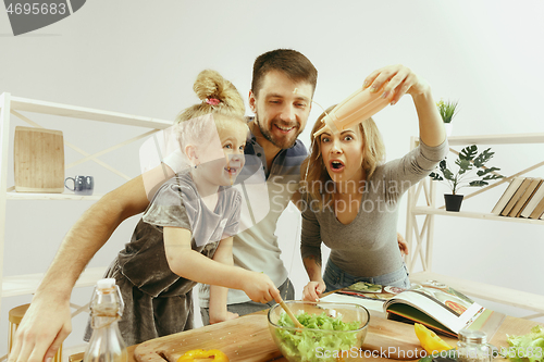 Image of Cute little girl and her beautiful parents are cutting vegetables in kitchen at home