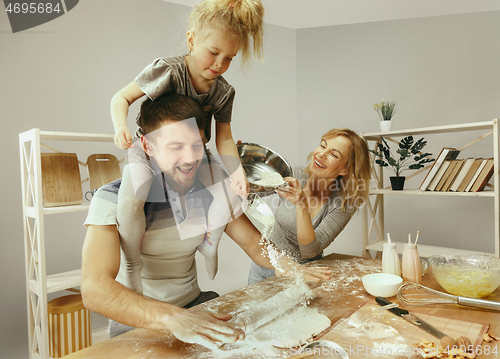 Image of Cute little girl and her beautiful parents preparing the dough for the cake in kitchen at home