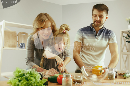 Image of Cute little girl and her beautiful parents are cutting vegetables in kitchen at home