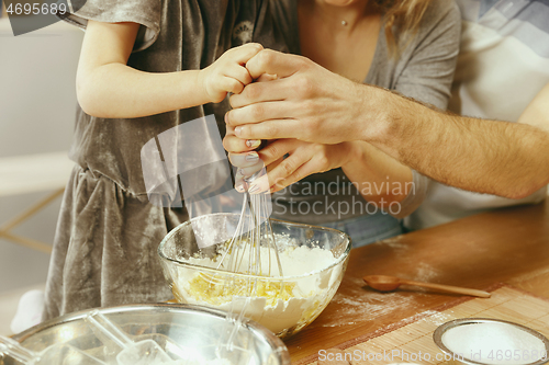 Image of Cute little girl and her beautiful parents preparing the dough for the cake in kitchen at home