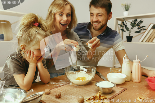 Image of Cute little girl and her beautiful parents preparing the dough for the cake in kitchen at home