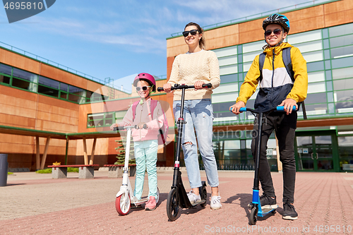 Image of happy school children with mother riding scooters