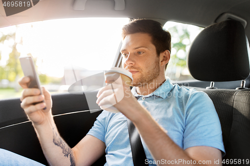 Image of passenger drinking coffee using smartphone in car