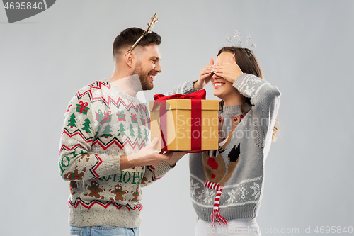 Image of happy couple in christmas sweaters with gift box