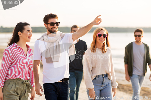 Image of happy friends walking along summer beach