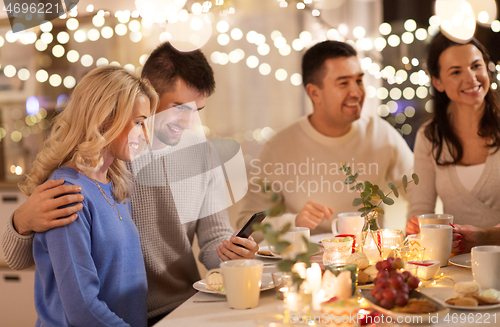 Image of happy friends with smartphone at tea party at home