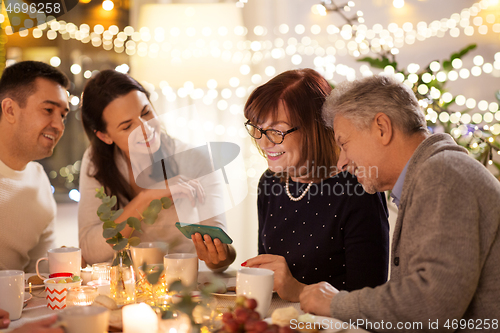 Image of happy family with smartphone at tea party at home