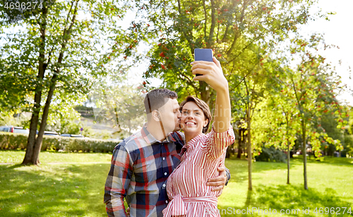 Image of happy couple in park taking selfie by smartphone