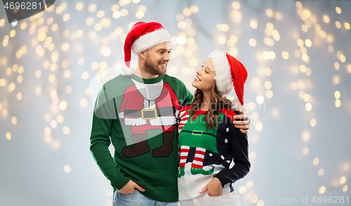 Image of happy couple in christmas sweaters and santa hats