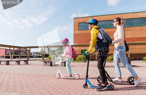 Image of happy school children with mother riding scooters