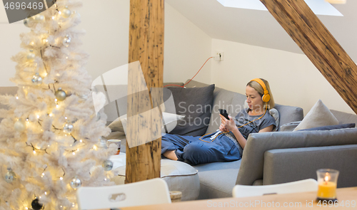 Image of Young thoughtful woman sitting indoors at home living room sofa using social media on phone for video chatting and staying connected with her loved ones. Stay at home, social distancing lifestyle