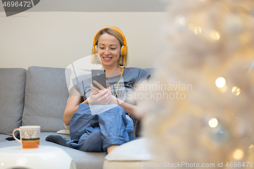 Image of Young cheerful woman sitting indoors at home living room sofa using social media on phone for video chatting and staying connected with her loved ones. Stay at home, social distancing lifestyle