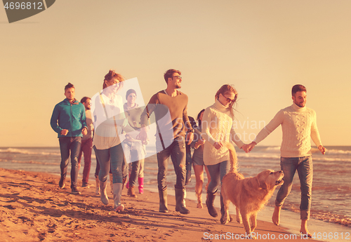 Image of Group of friends running on beach during autumn day