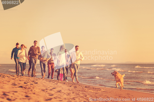 Image of Group of friends running on beach during autumn day