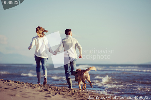 Image of couple with dog having fun on beach on autmun day