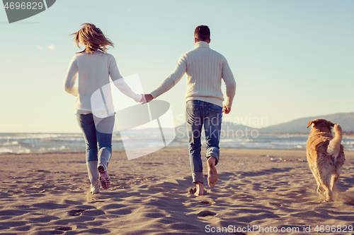 Image of couple with dog having fun on beach on autmun day