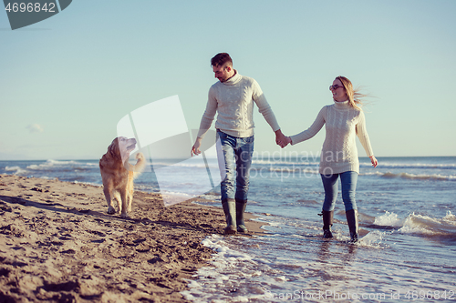 Image of couple with dog having fun on beach on autmun day