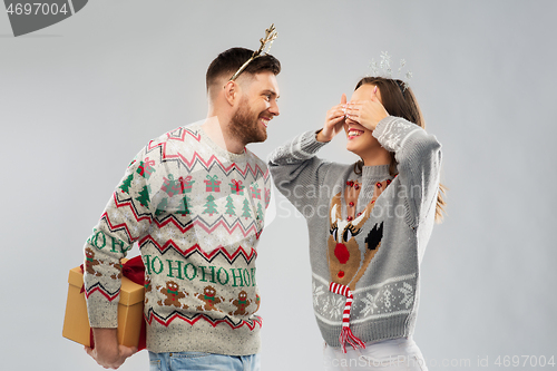 Image of happy couple in christmas sweaters with gift box